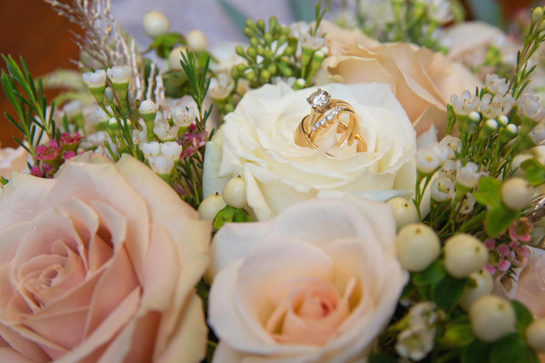 wedding rings sit inside a bouquet of white and peach roses