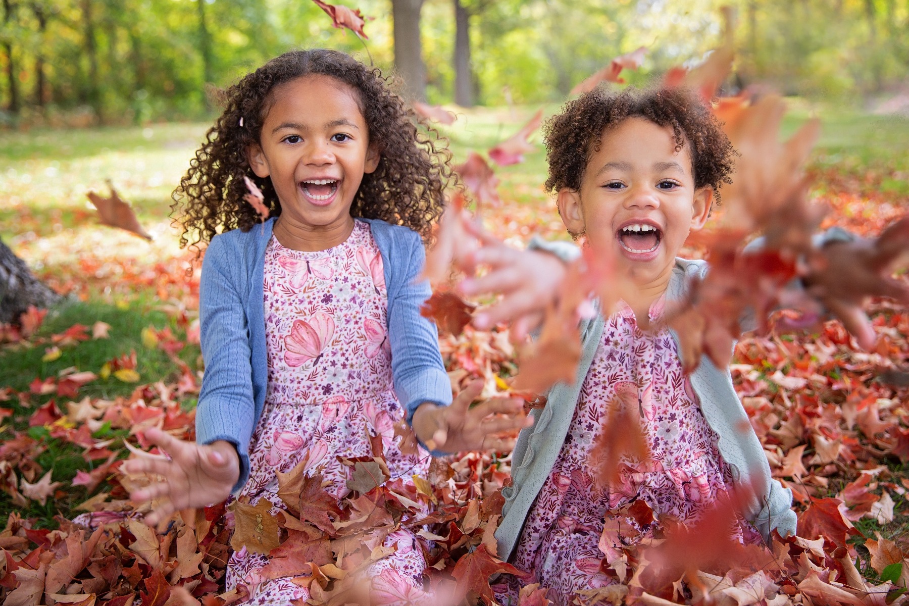 two curled haired girls laugh and throw fall leaves at the camera