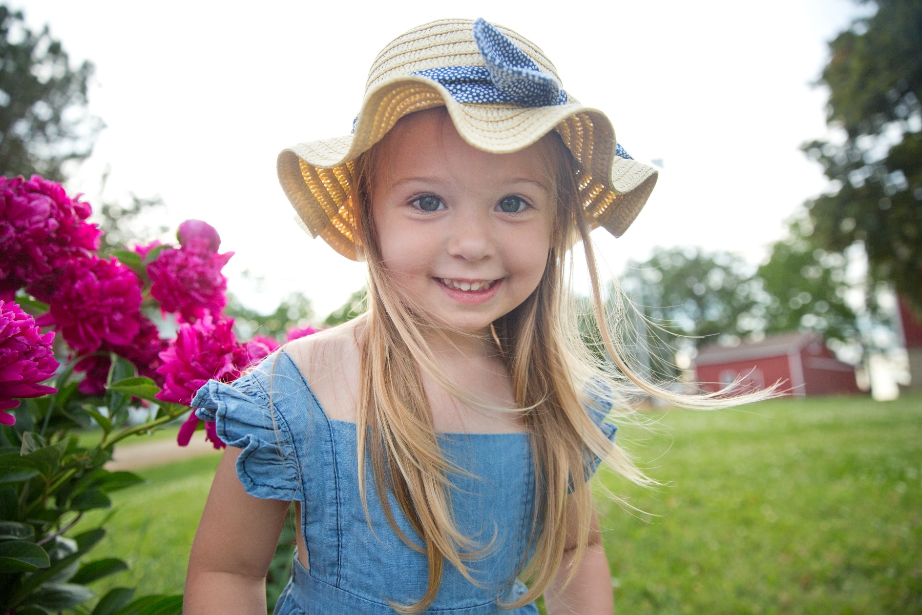 little girl with blonde hair and a straw hat by pink peonies