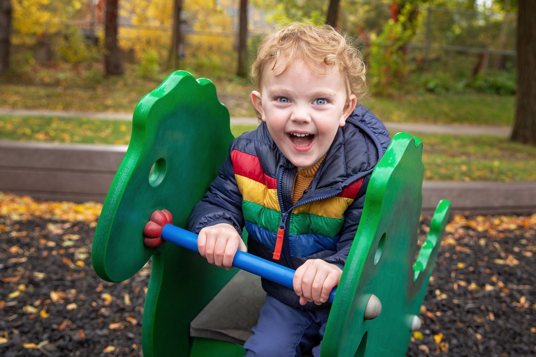 blond haired boy plays on a green playground rocker