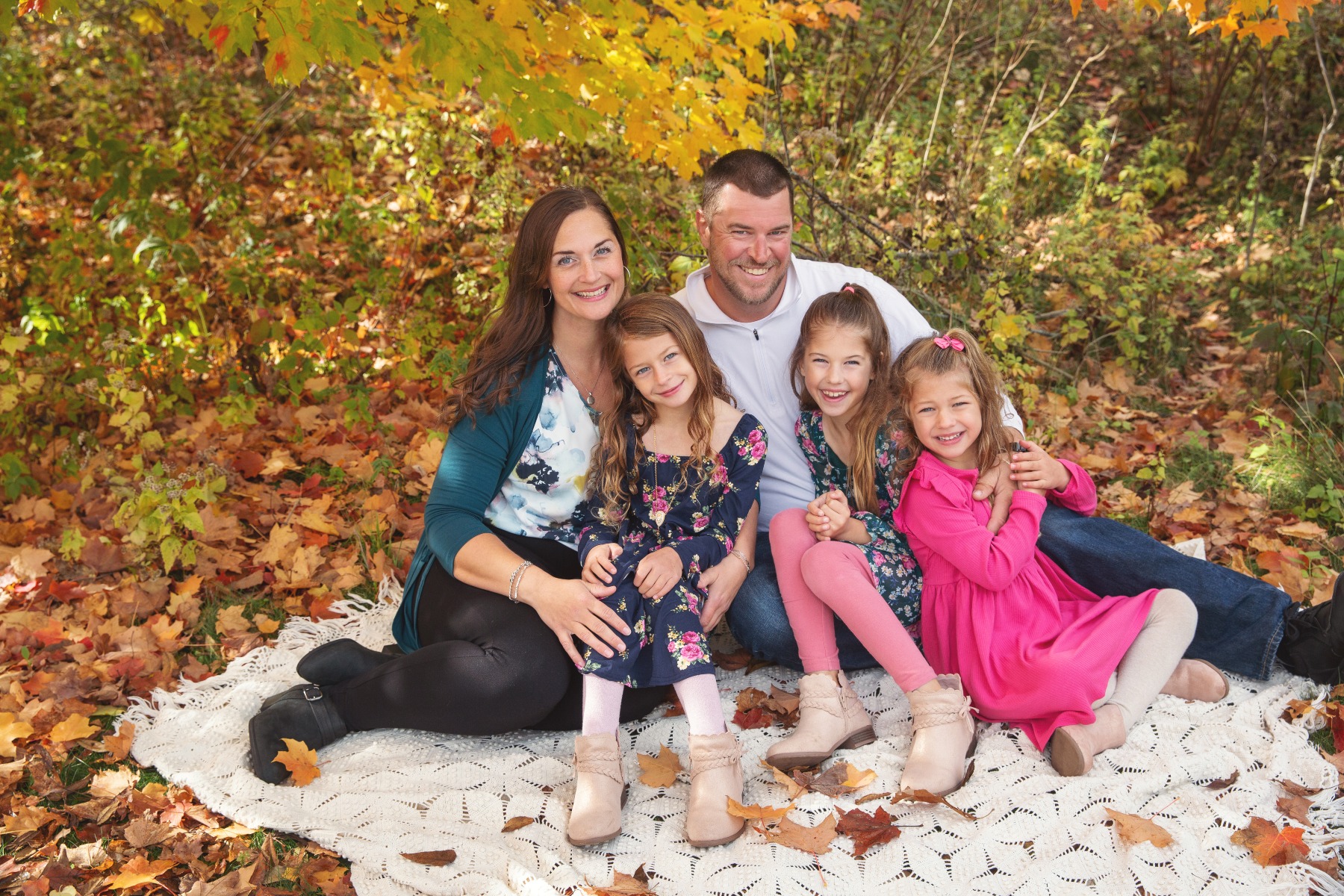 mom & dad and three young girls smile for a family photo in fall leaves