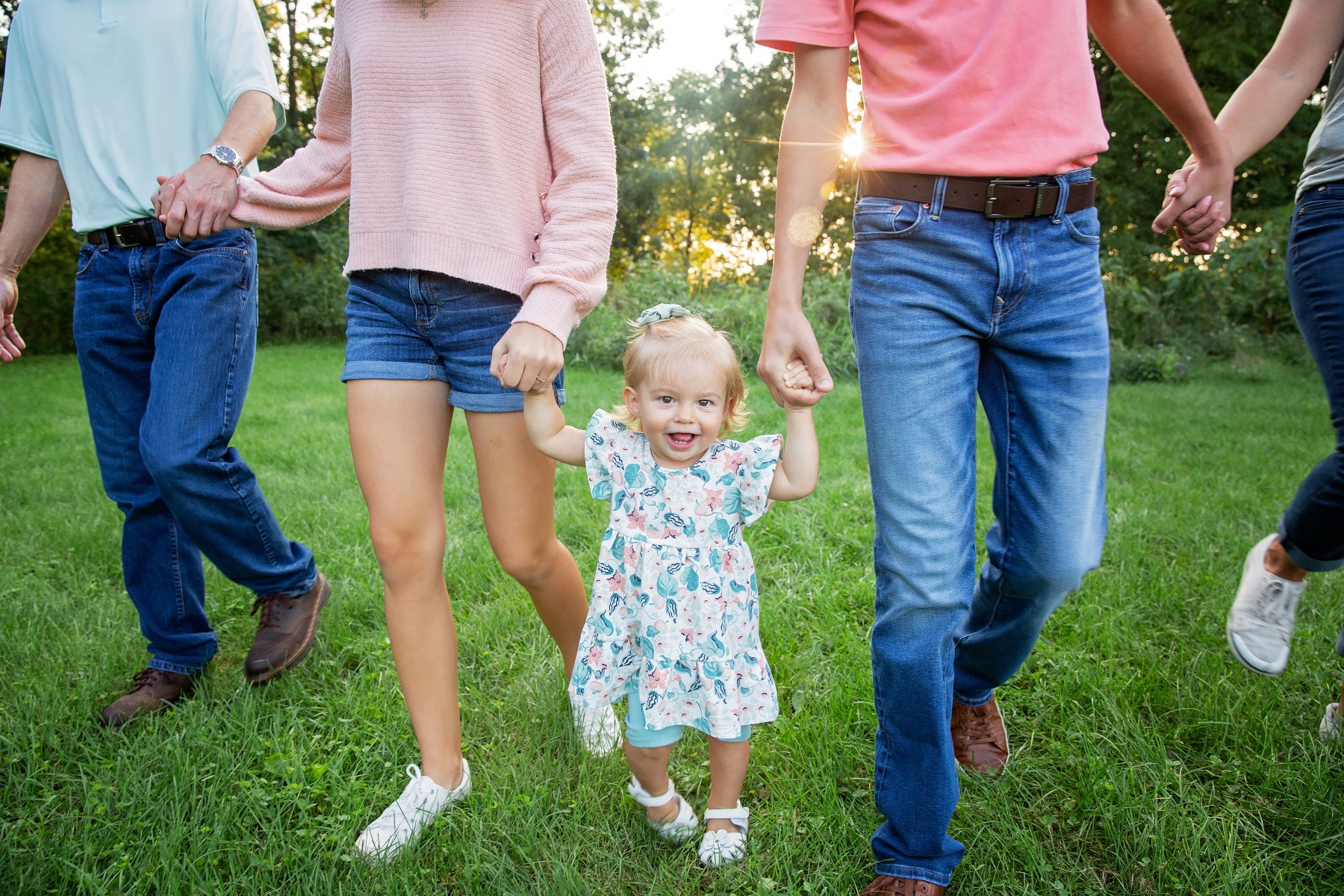 blond haired toddler walks holding hands with her family