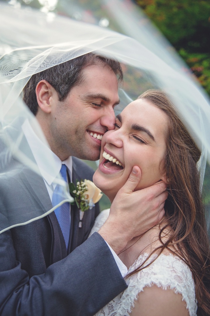 bride and groom laughing beneath her blowing veil