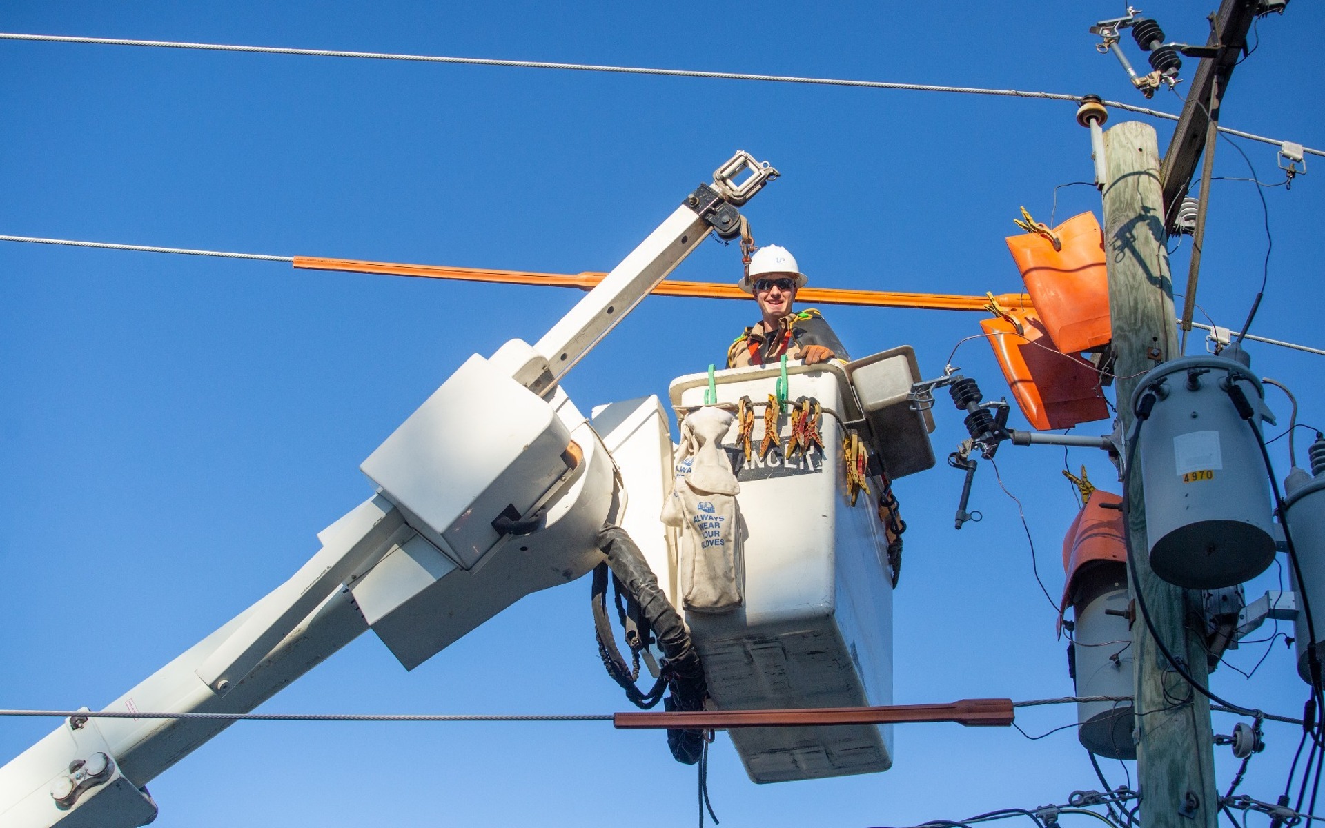 electric line worker smiles down from a basket working on a power line