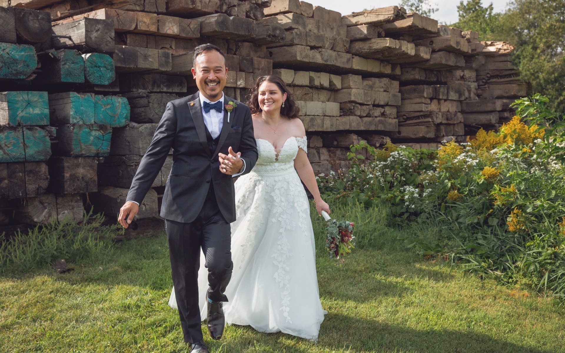groom in black tux, bride in white laughing as they walk together