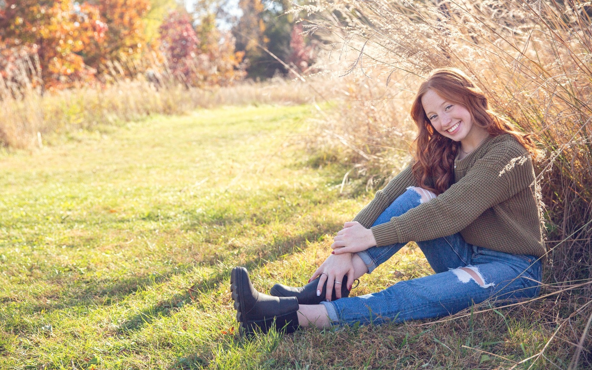 red headed hs senior girl poses by a field of fall grasses