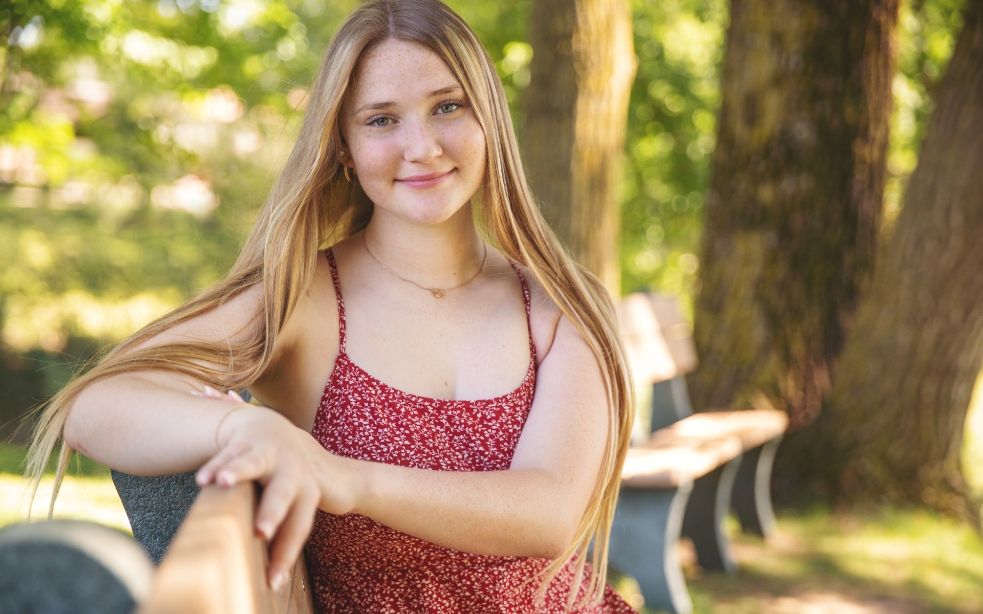 blond long haired hs senior girl sits on a park bench