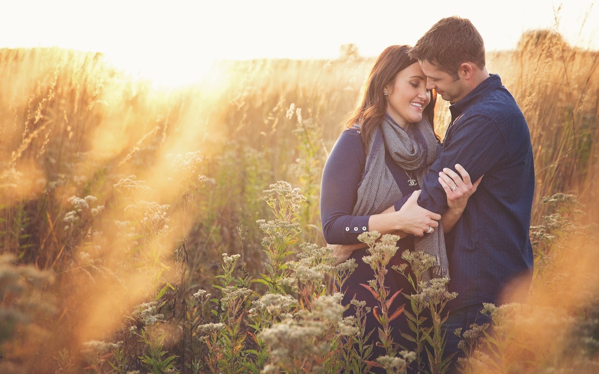 couple embrace in a field of tall backlit grass