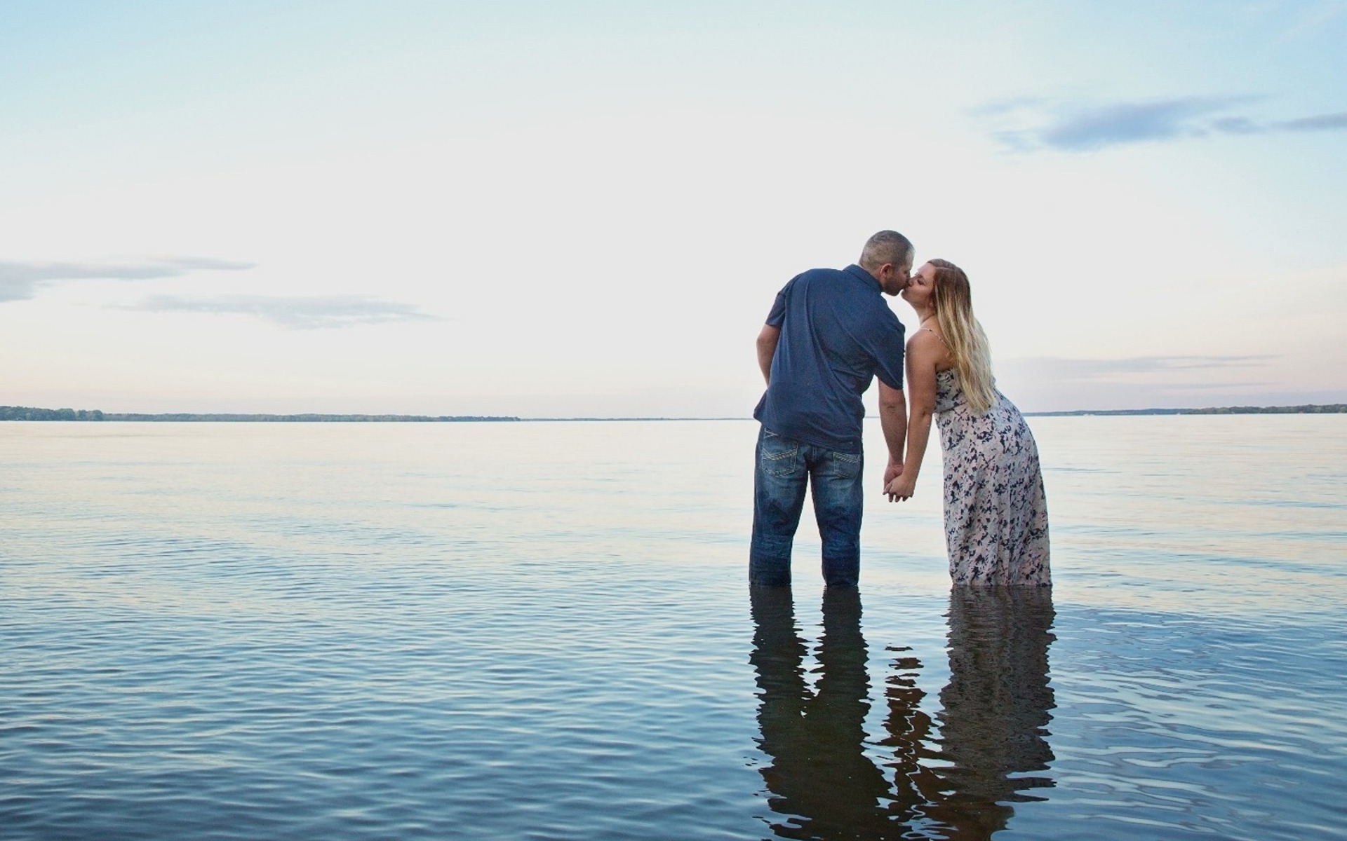 engaged couple stand in ankle deep water kissing