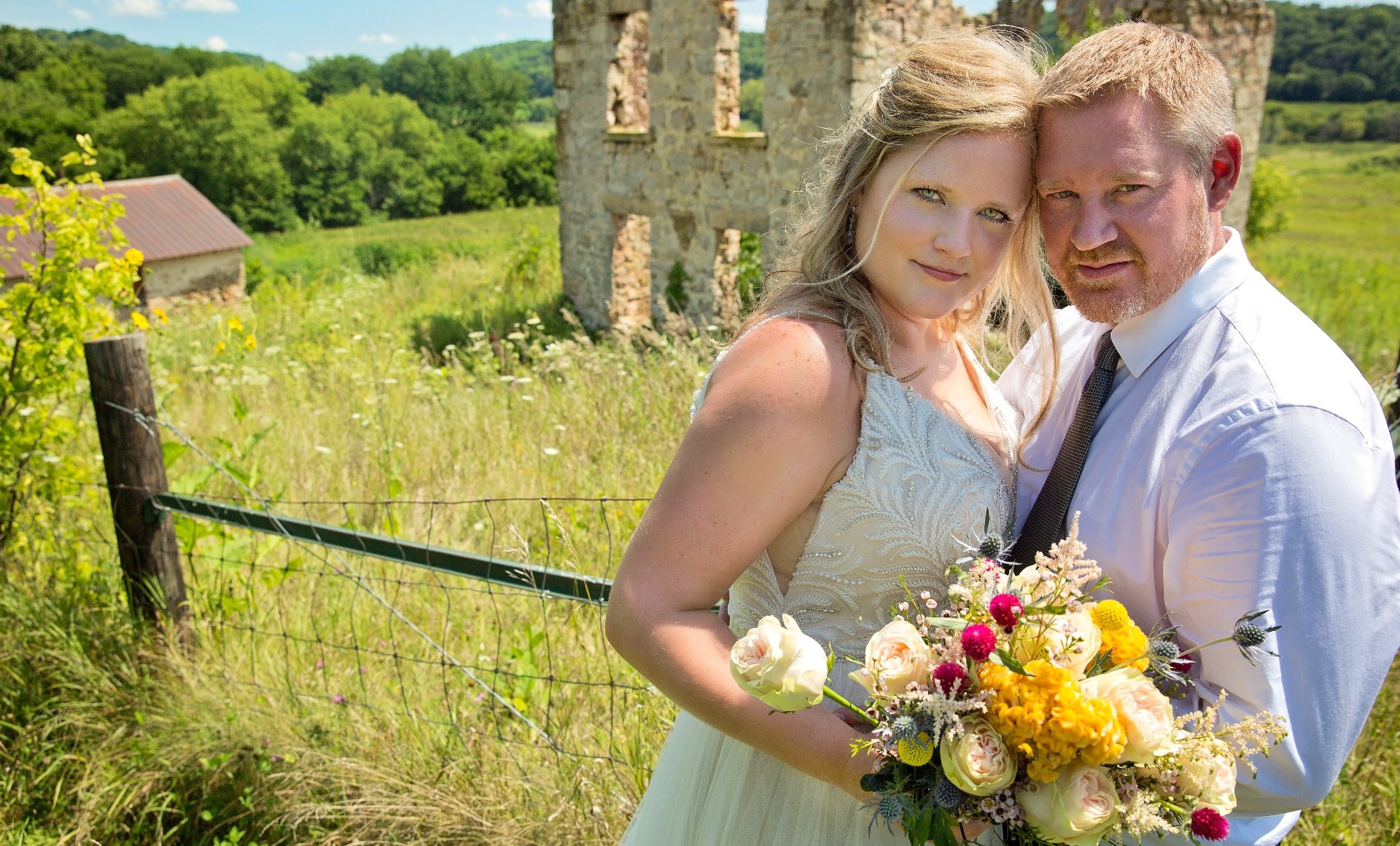 bride & groom pose for a photo in front of a stone farmhouse 