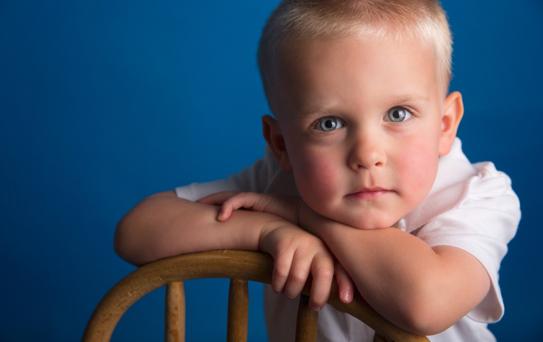 little boy with blue eyes poses in front of a blue background