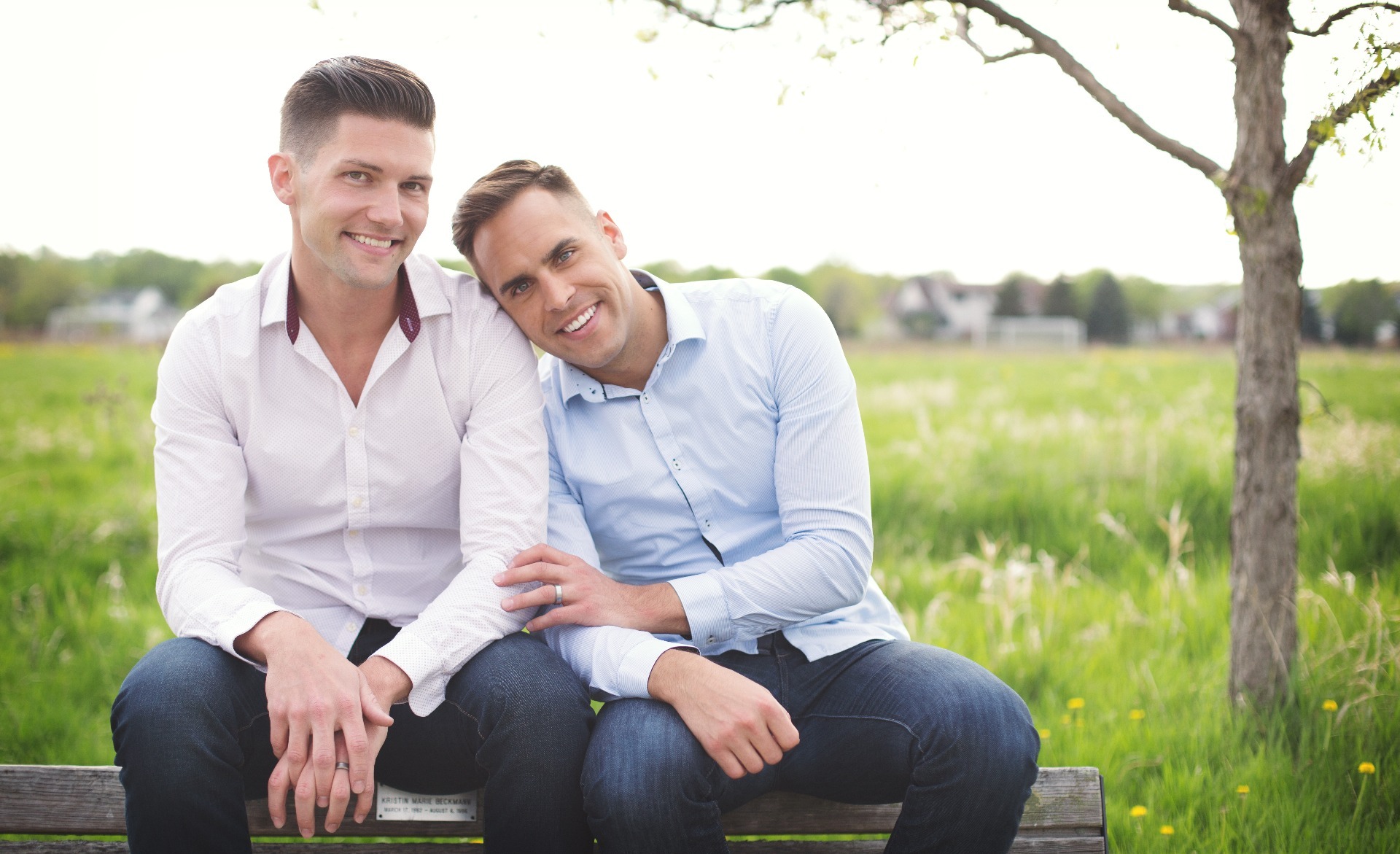 two men snuggle together on a wooden bench