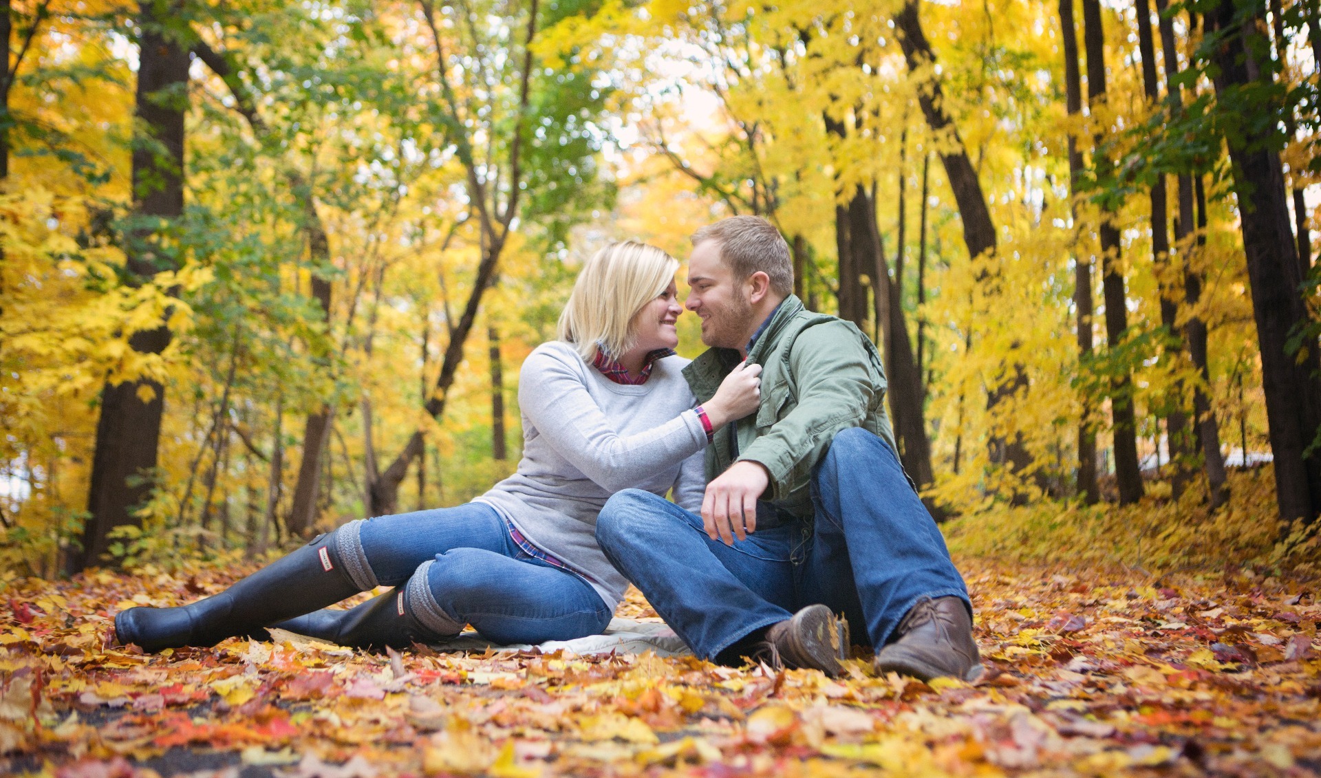 engaged couple sit amongst the fall leaves in a wood