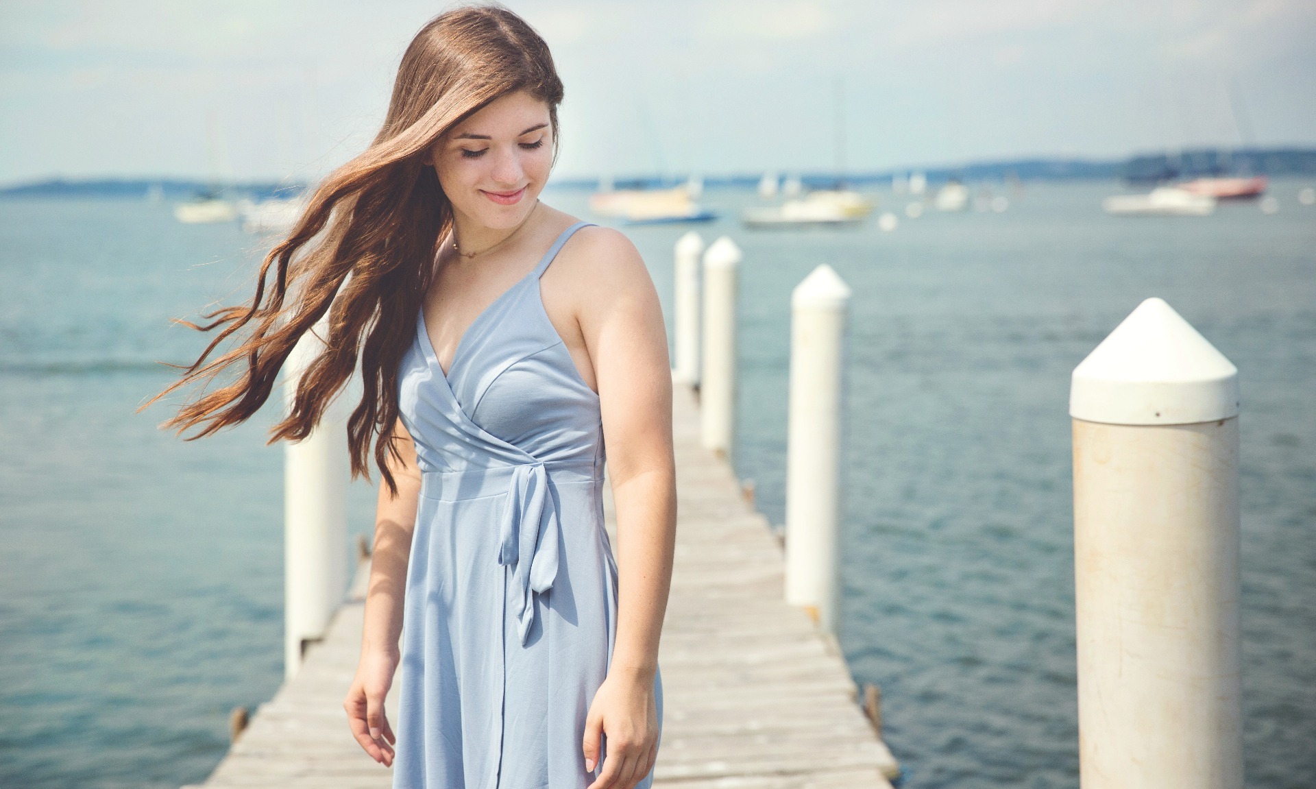 long haired senior girl stands on a white dock by the lake