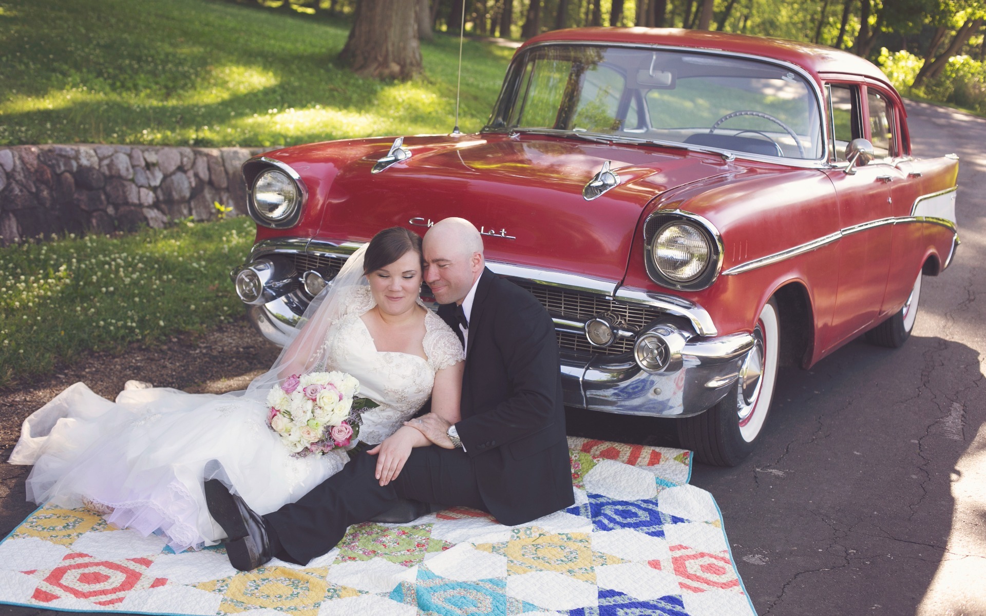 bride & groom snuggle on a blanket in front of a classic red chevrolet