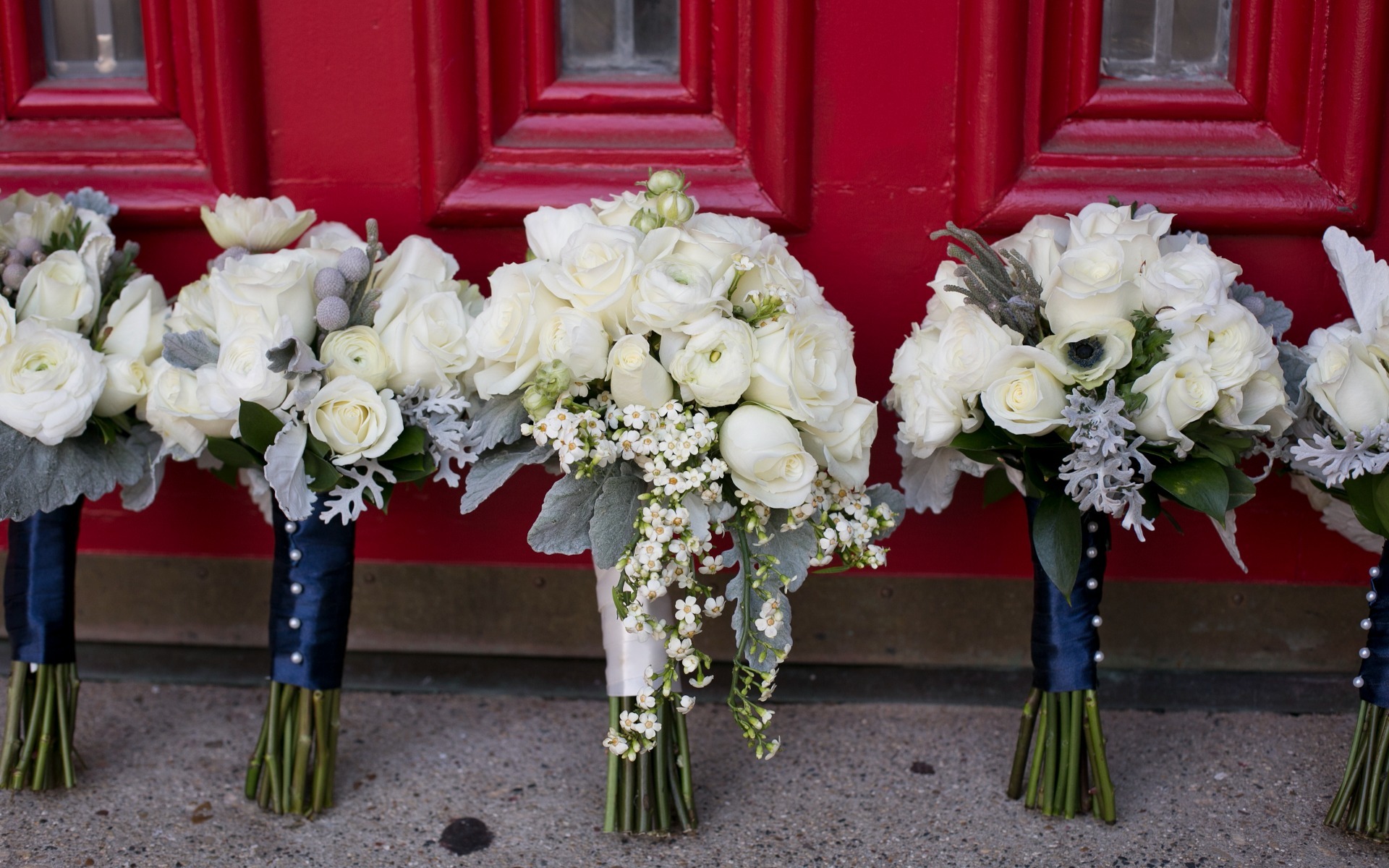 row of bridal bouquets of white lean against a red church door