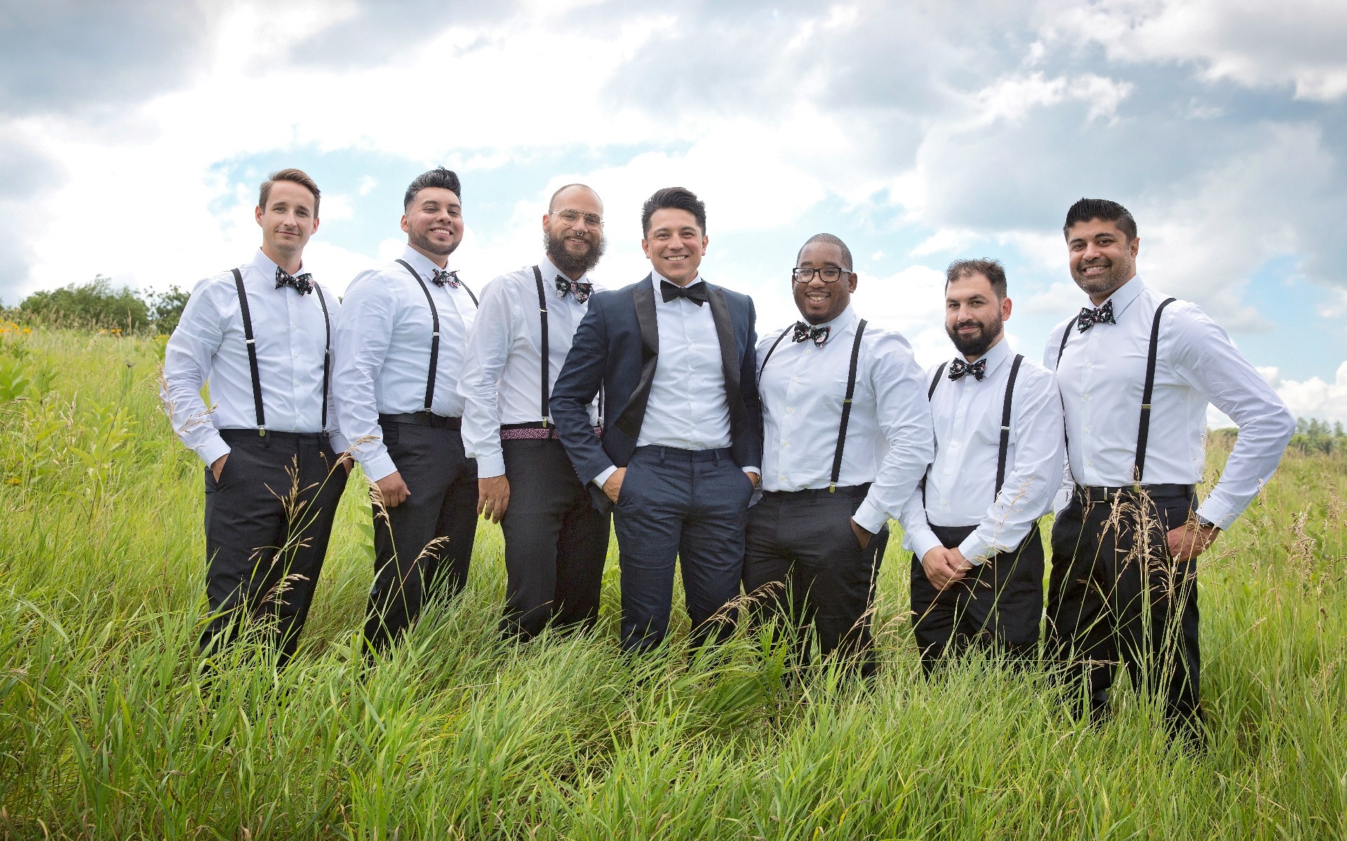 groom and 6 groomsmen stand in a tall grassy field