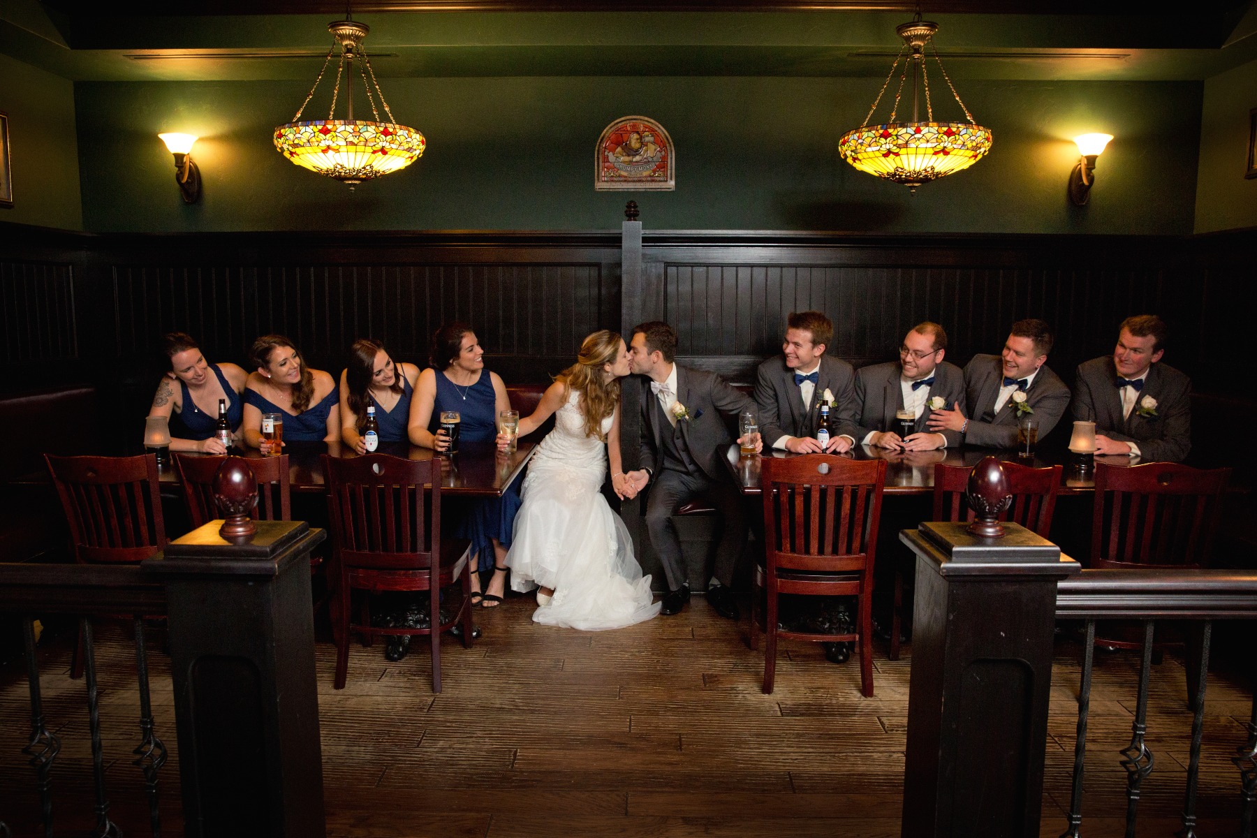 bride & groom kiss in a irish pub wooden booth while wedding party looks on