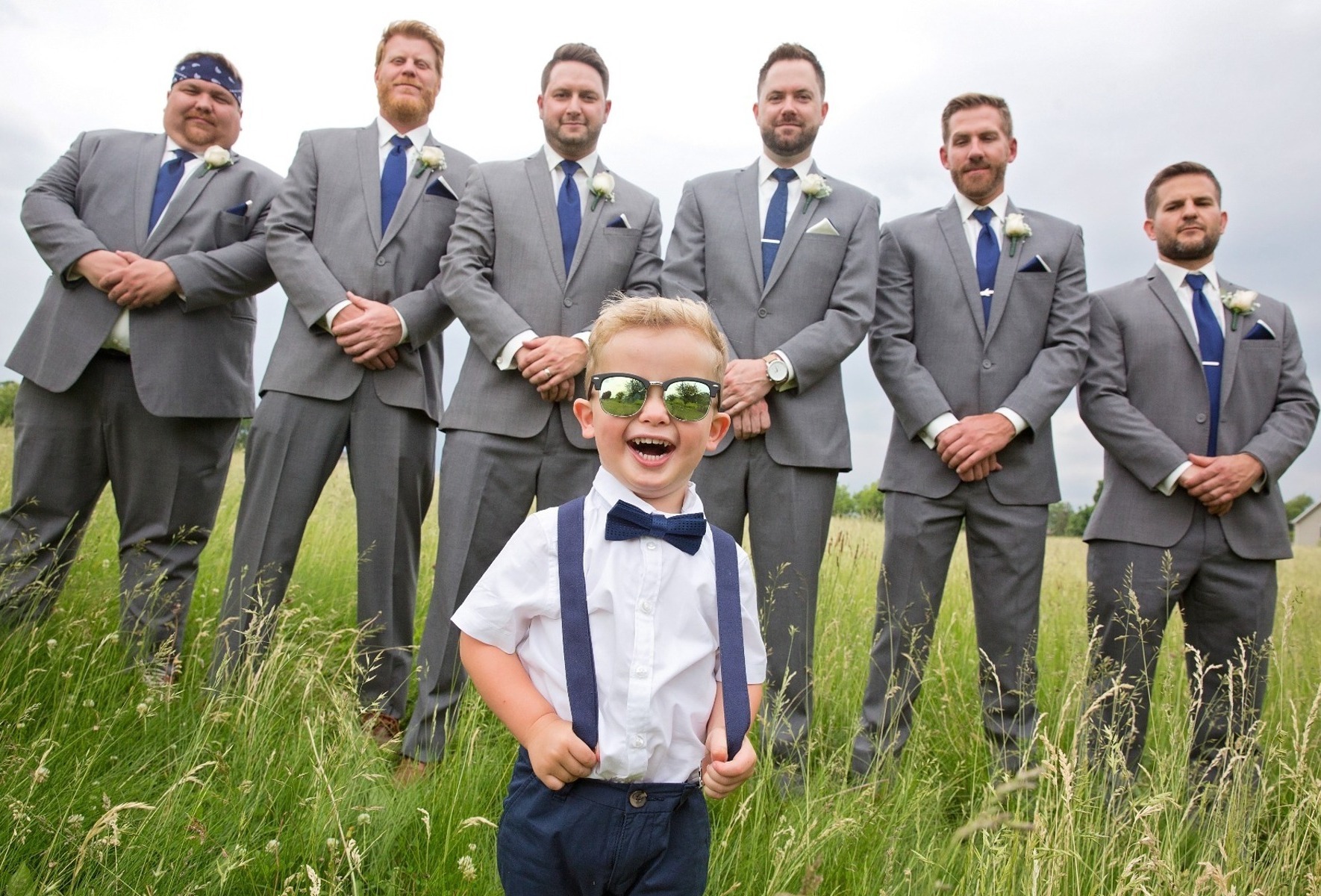 ring bearer laughs in front of a row of groomsmen