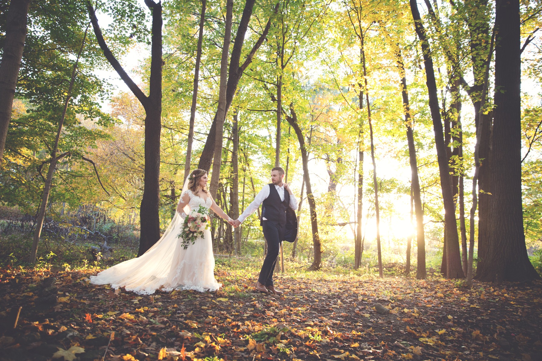 groom leads his bride through a yellow wooded forest