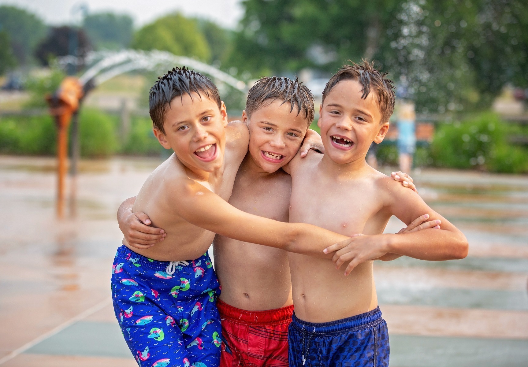 three brothers laugh and hug on a wet splash pad