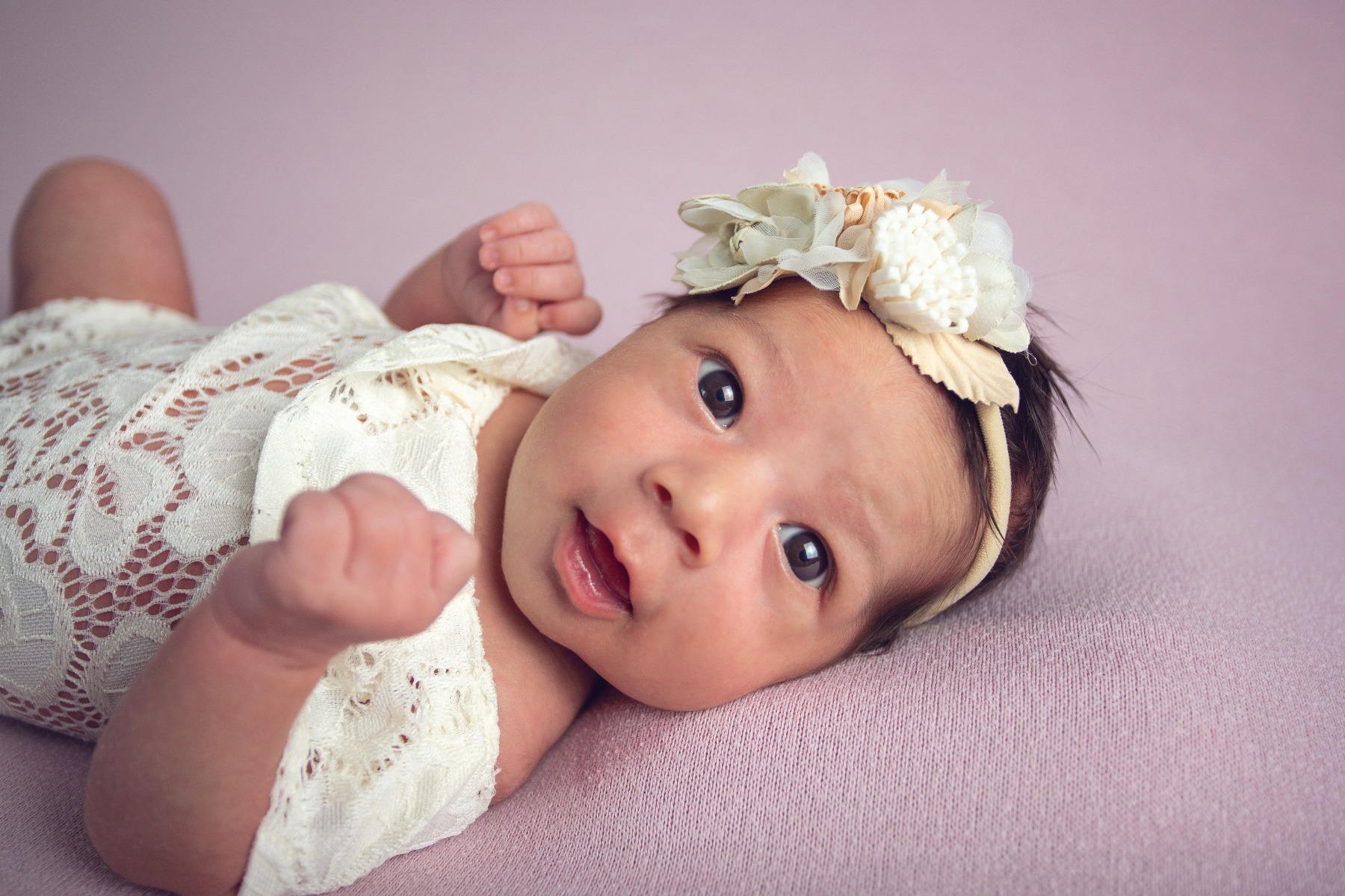 dark haired newborn baby smiles in a white romper