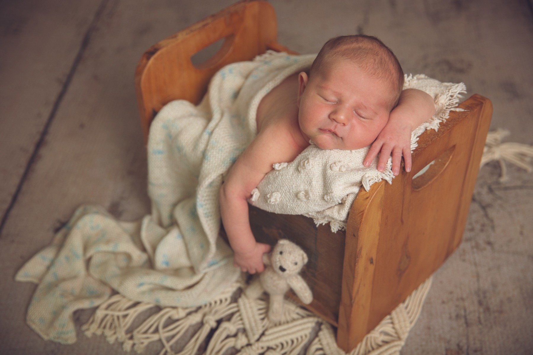newborn sleeping on his belly in a wooden bed, teddy bear in hand