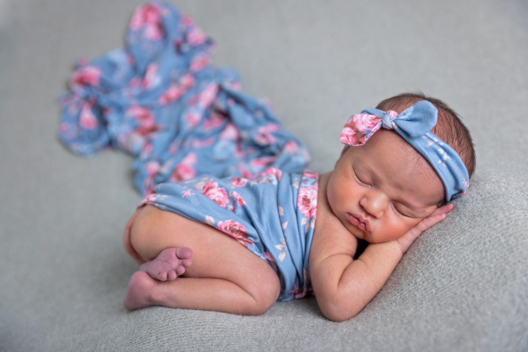 newborn sleeping on her belly with a blue & pink swaddle and headband
