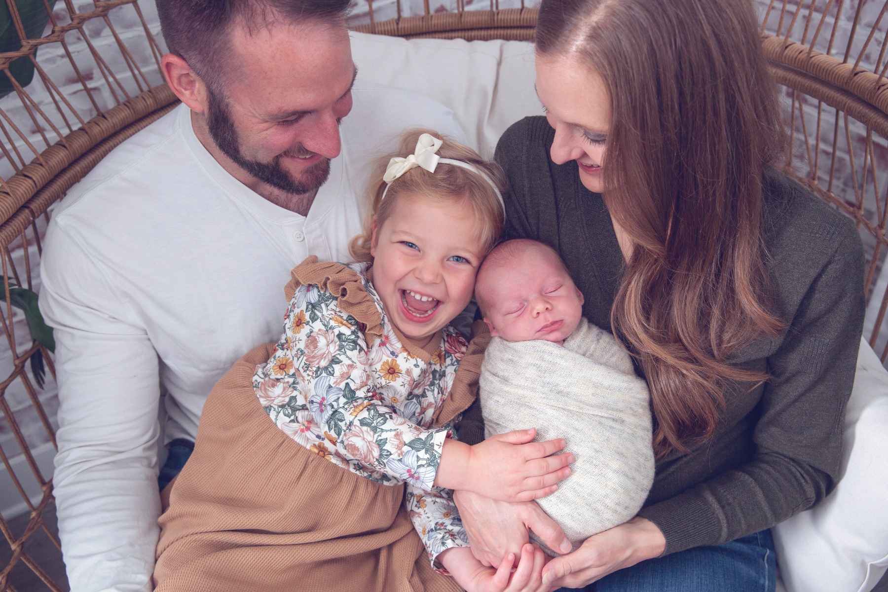 family of four with newborn sleeping baby, toddler sister is laughing