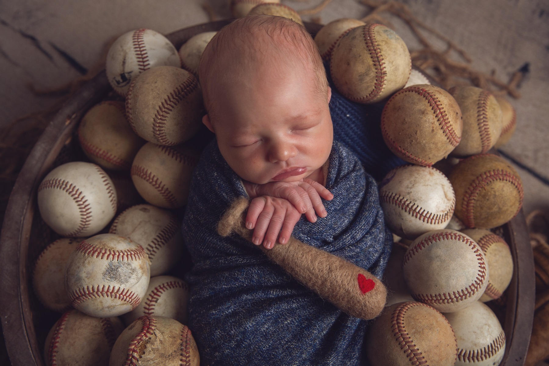 newborn baby swaddled sleeping amongst vintage baseballs