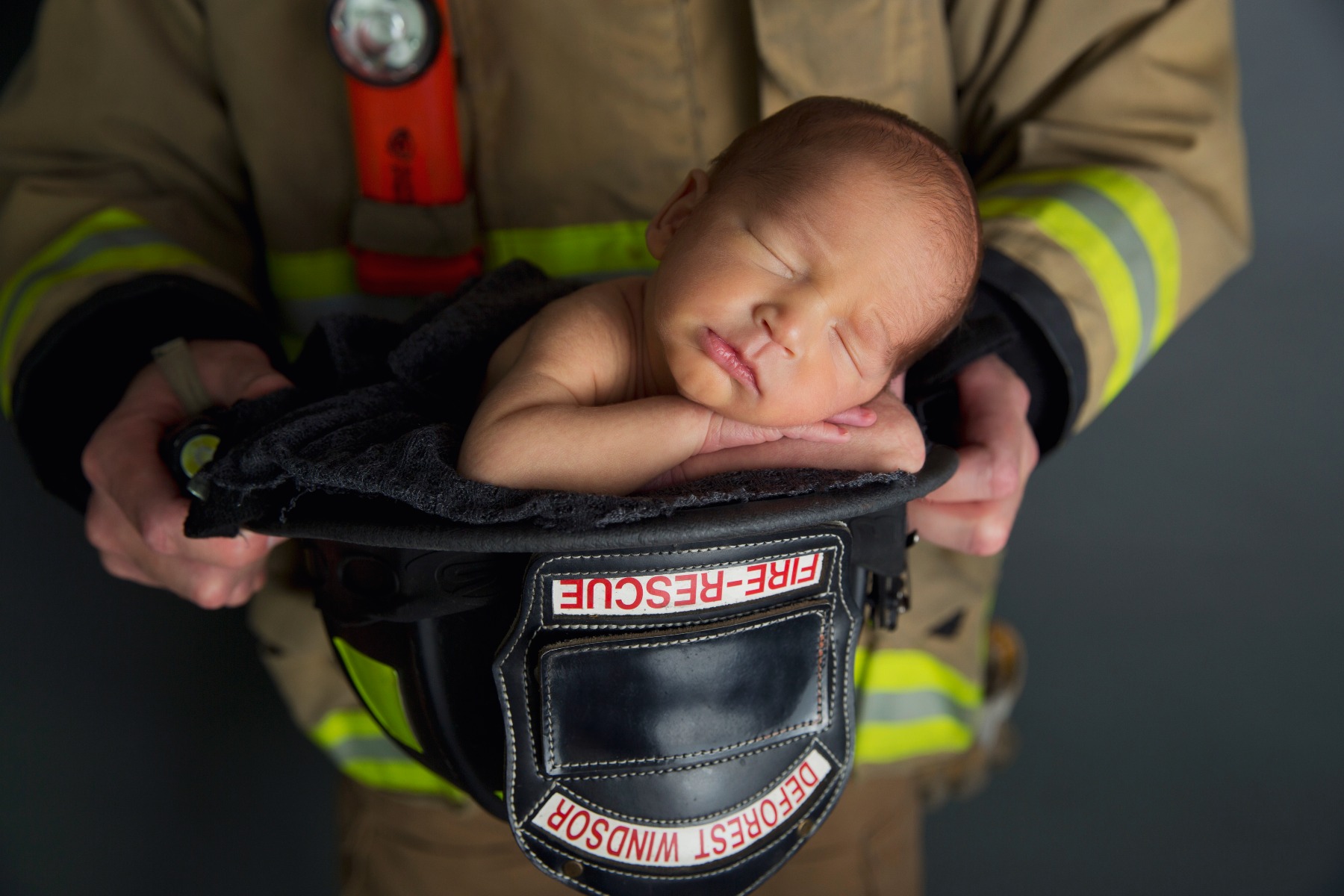 newborn baby sleeping in a firefighter's helmut held in dad's hands