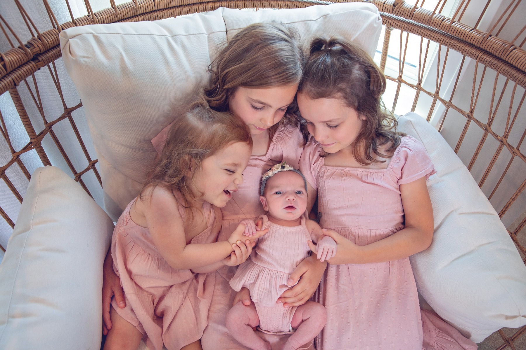 newborn baby girl being adored by her three older sisters all in pink
