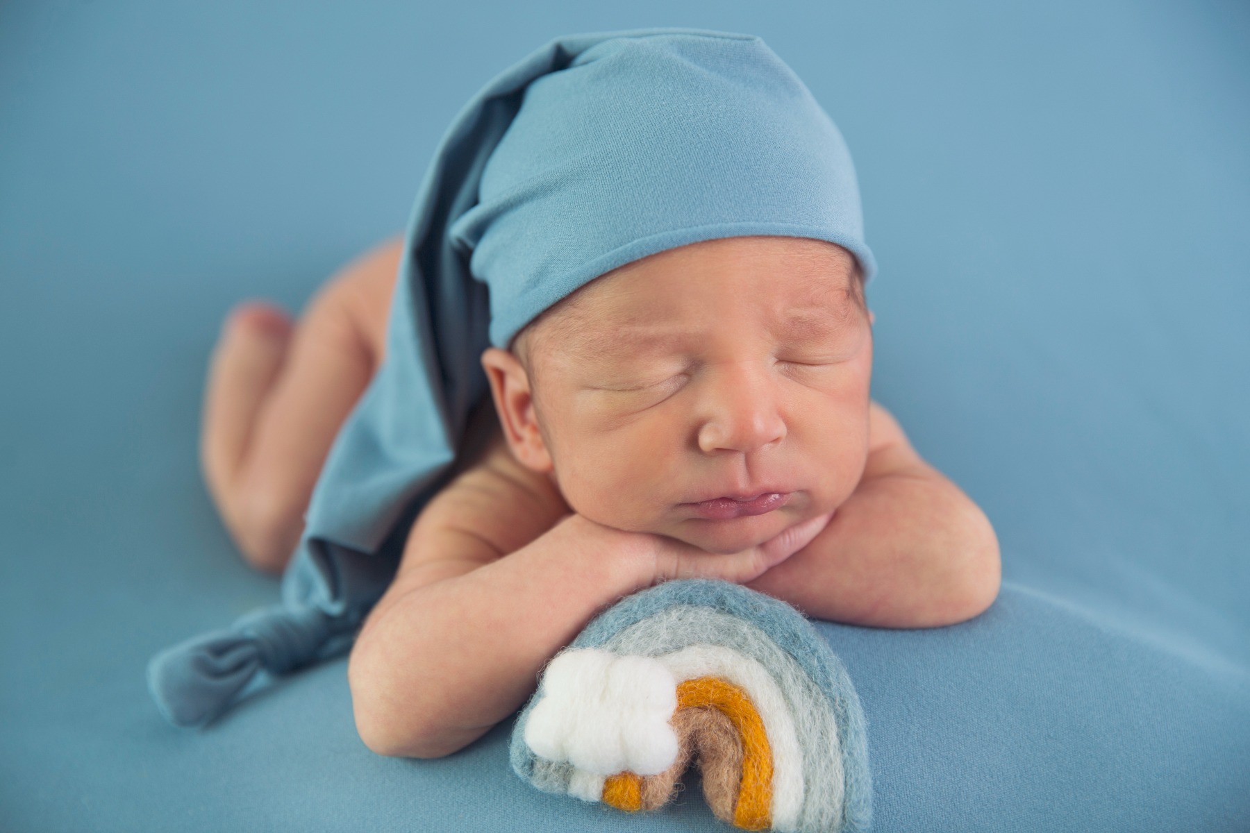 newborn baby with blue stocking hat and a felted rainbow