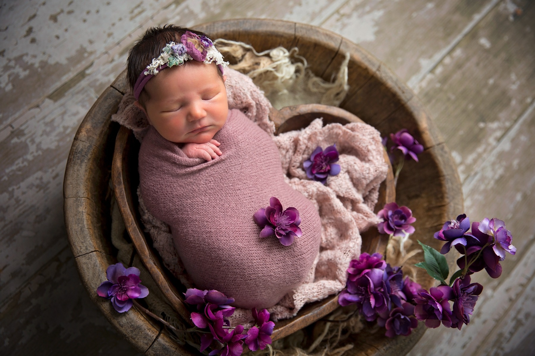 sleeping newborn in a heart shaped bowl with purple flowers