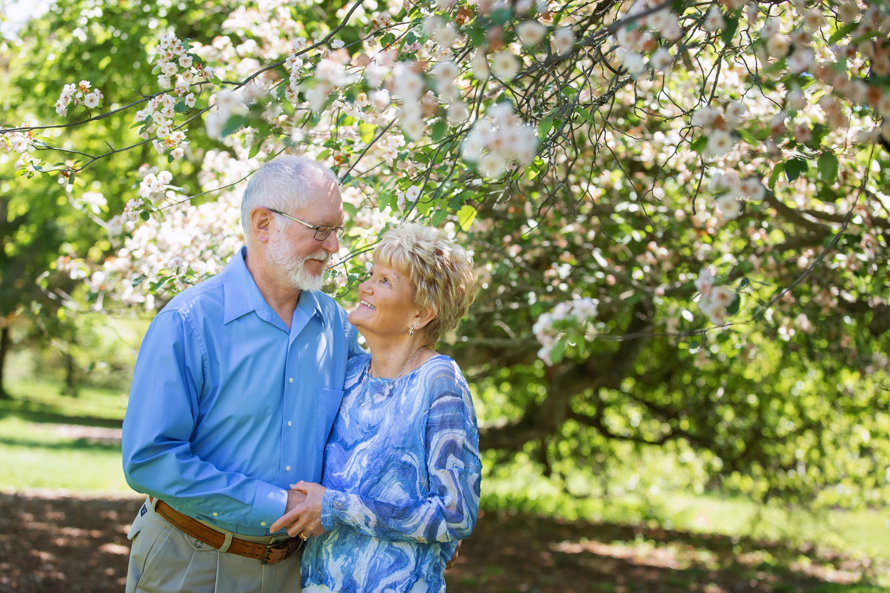 retired couple look at each other under a white cherry tree