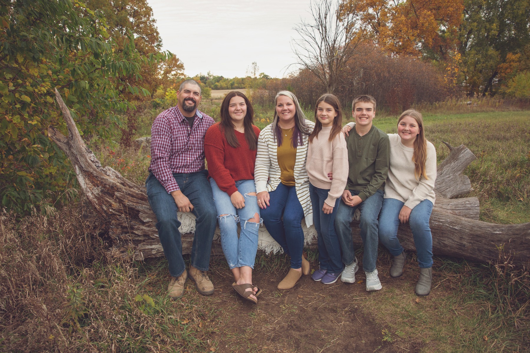 family of 6 pose for a photo on a tree log in a fall setting
