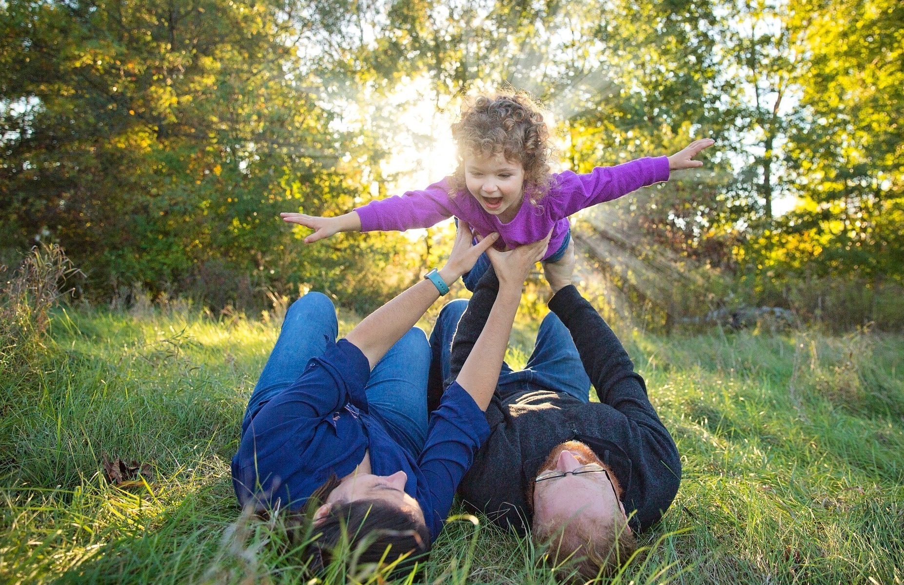 parents lay on their backs flying a little girl in the air above them