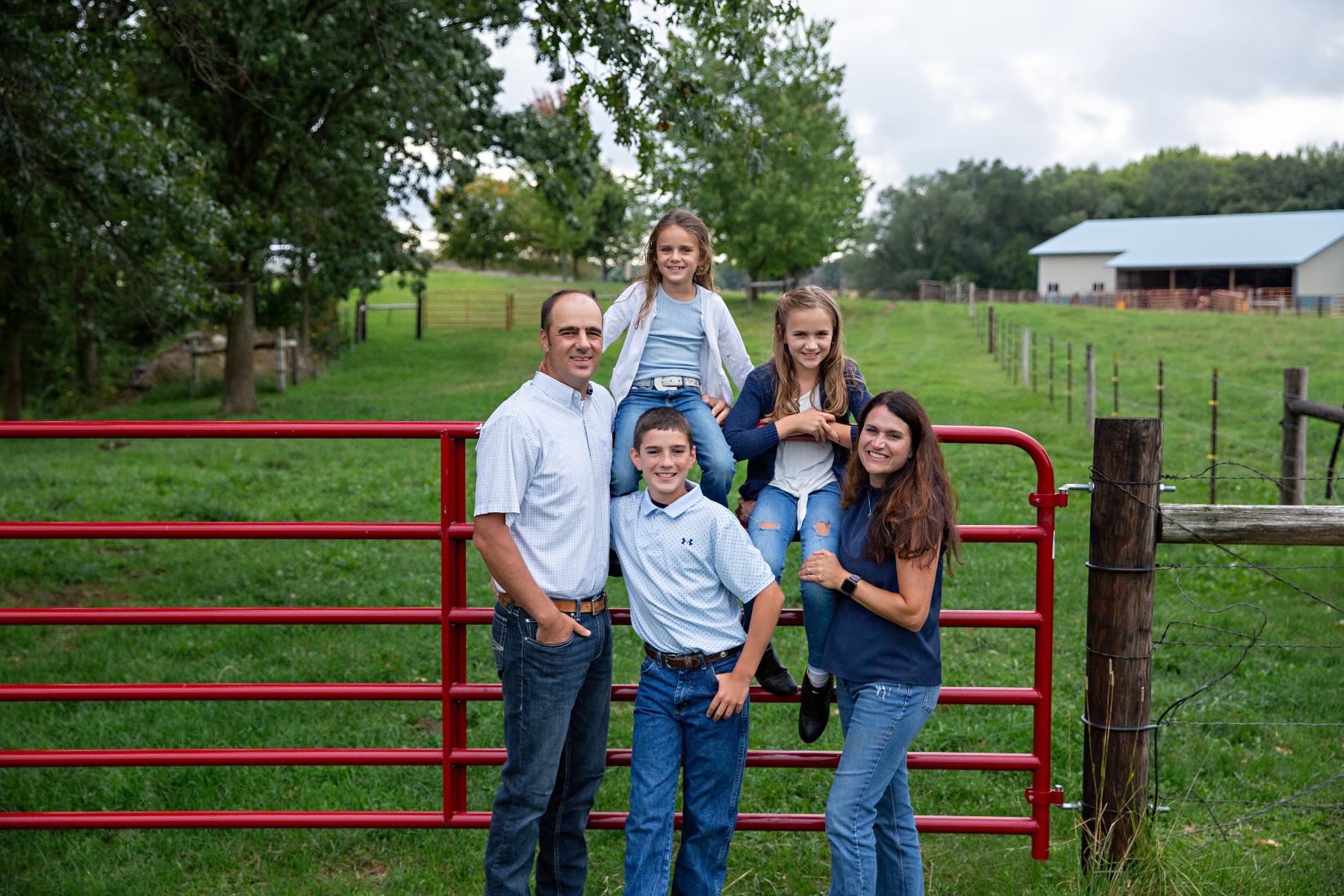 family of 5 pose on a red gate for a family photo on their farm