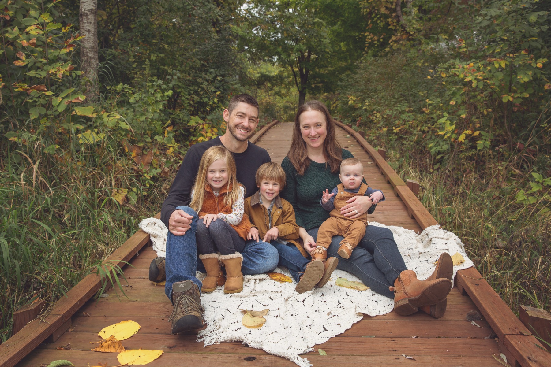 young family of 5 sit together on a wooden boardwalk