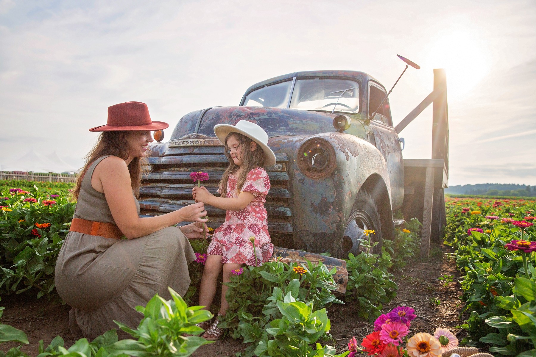 mom & young daughter in cowboy hats share flowers in front of a vintage truck