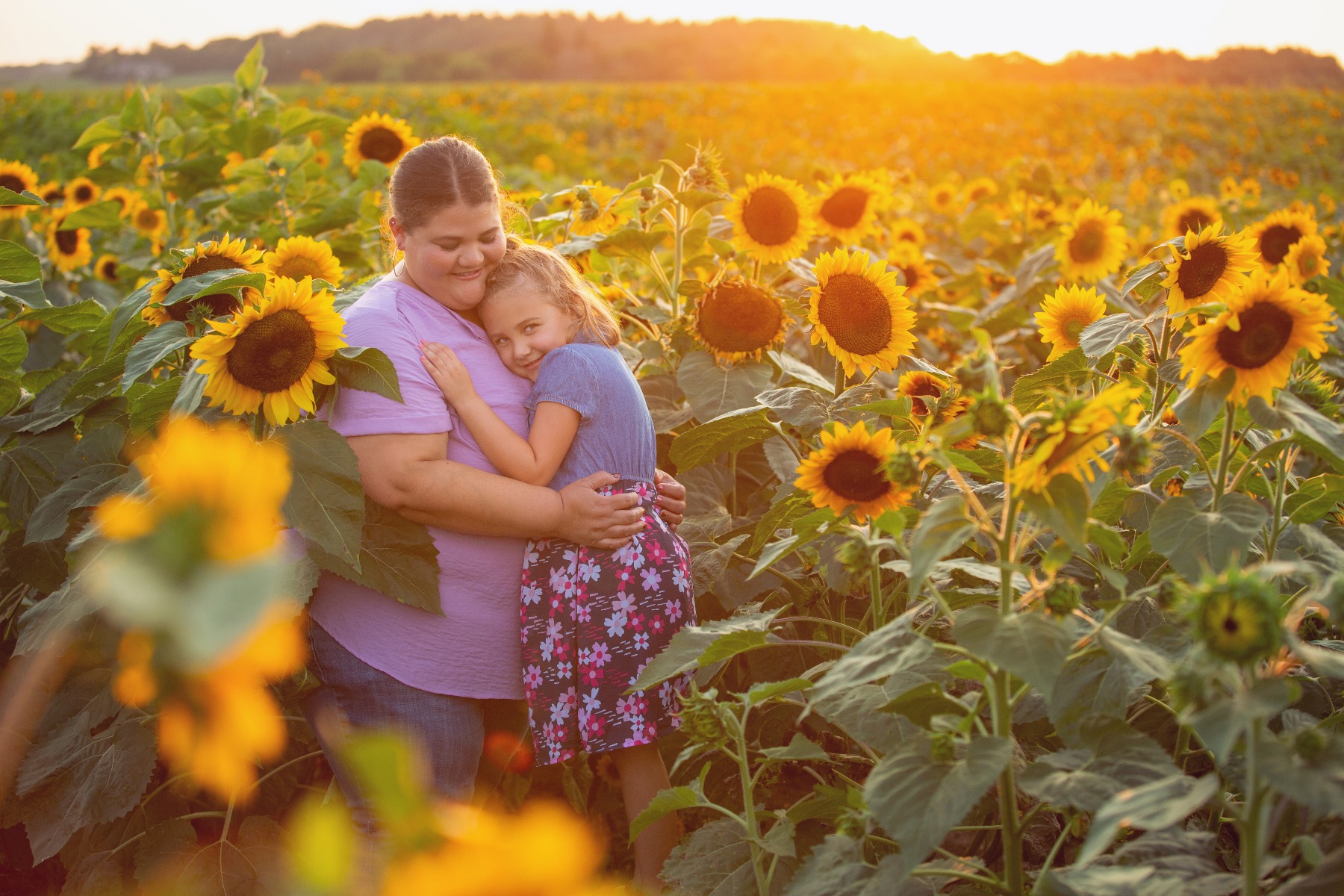 mom and daughter snuggle in a field of sunflowers
