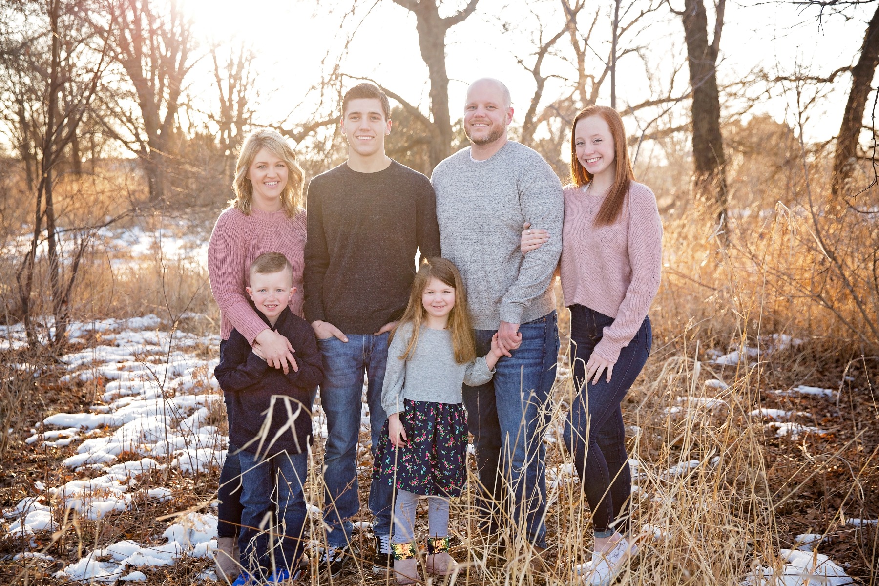 family of 6 pose in a snow covered field with tall grasses