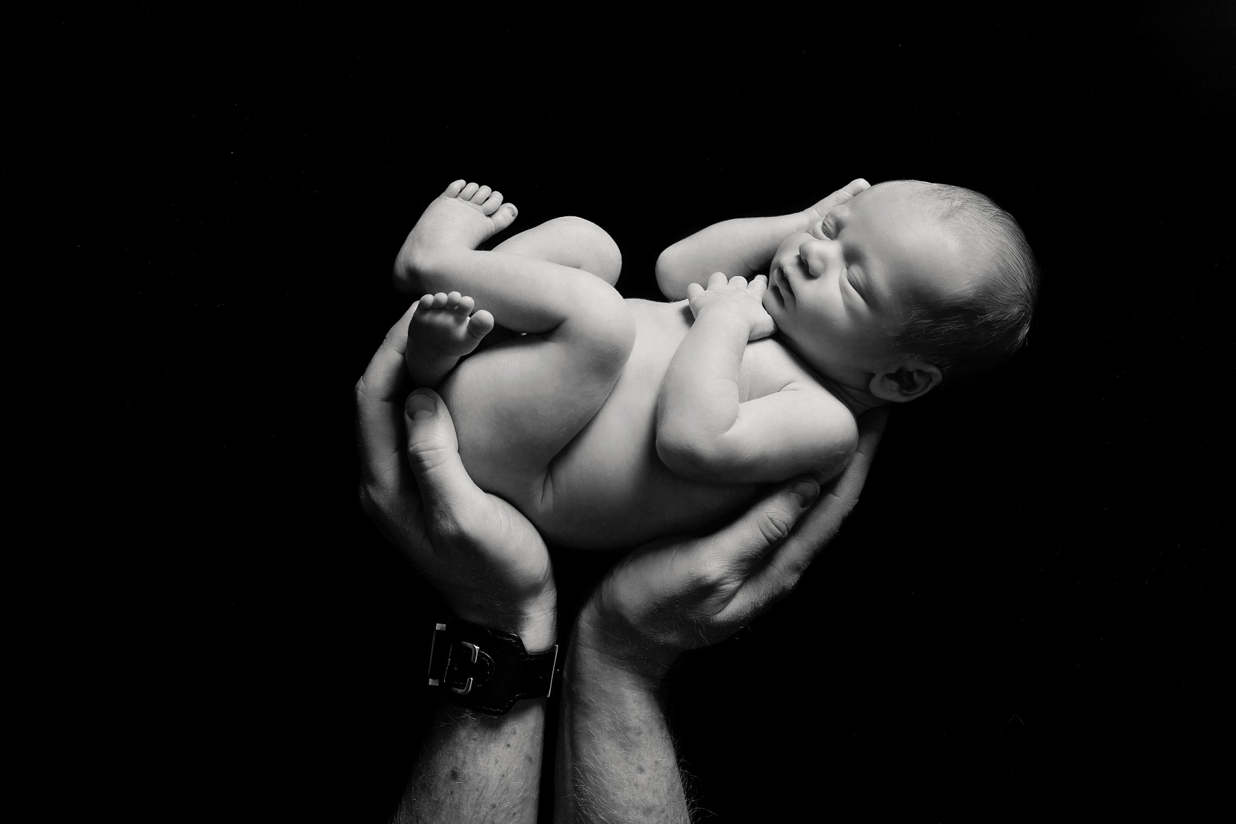 b&w photo of newborn in dad's hands