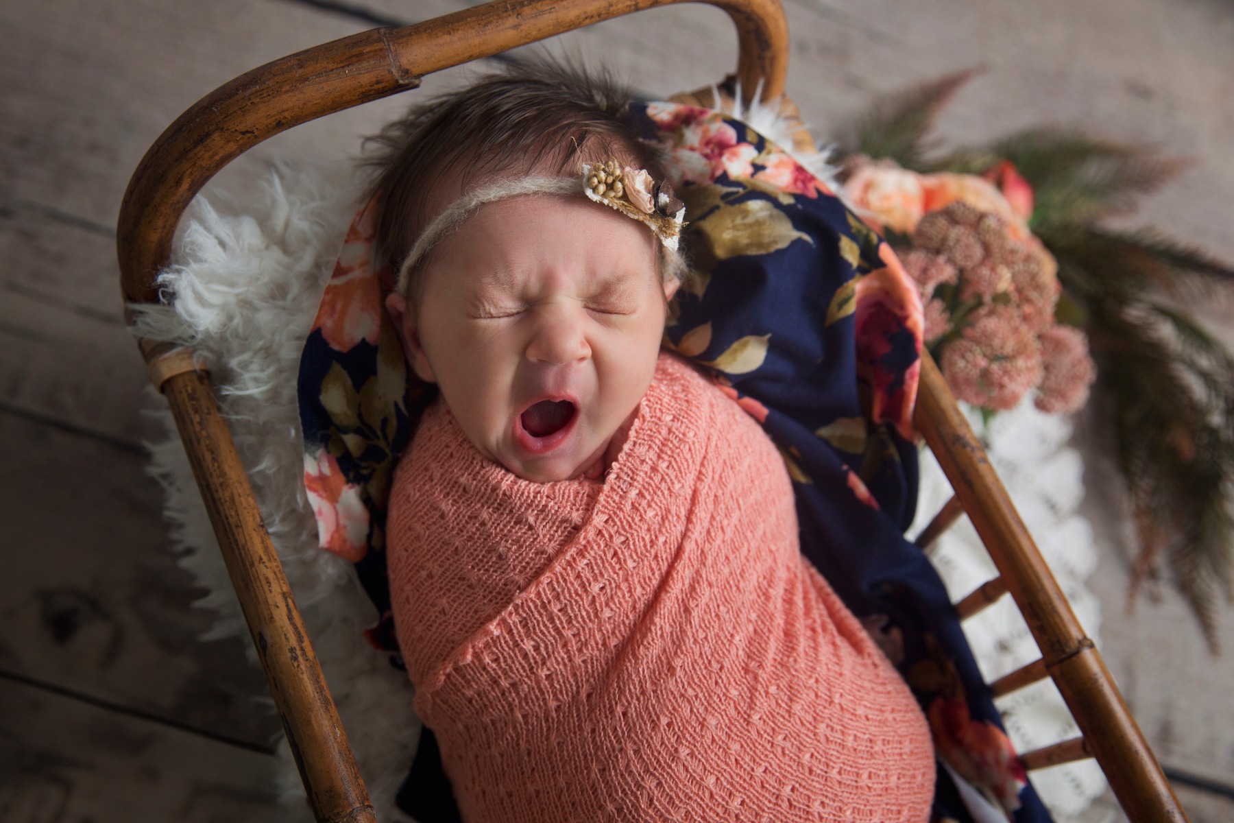 newborn baby swaddled in peach yawns in a crib