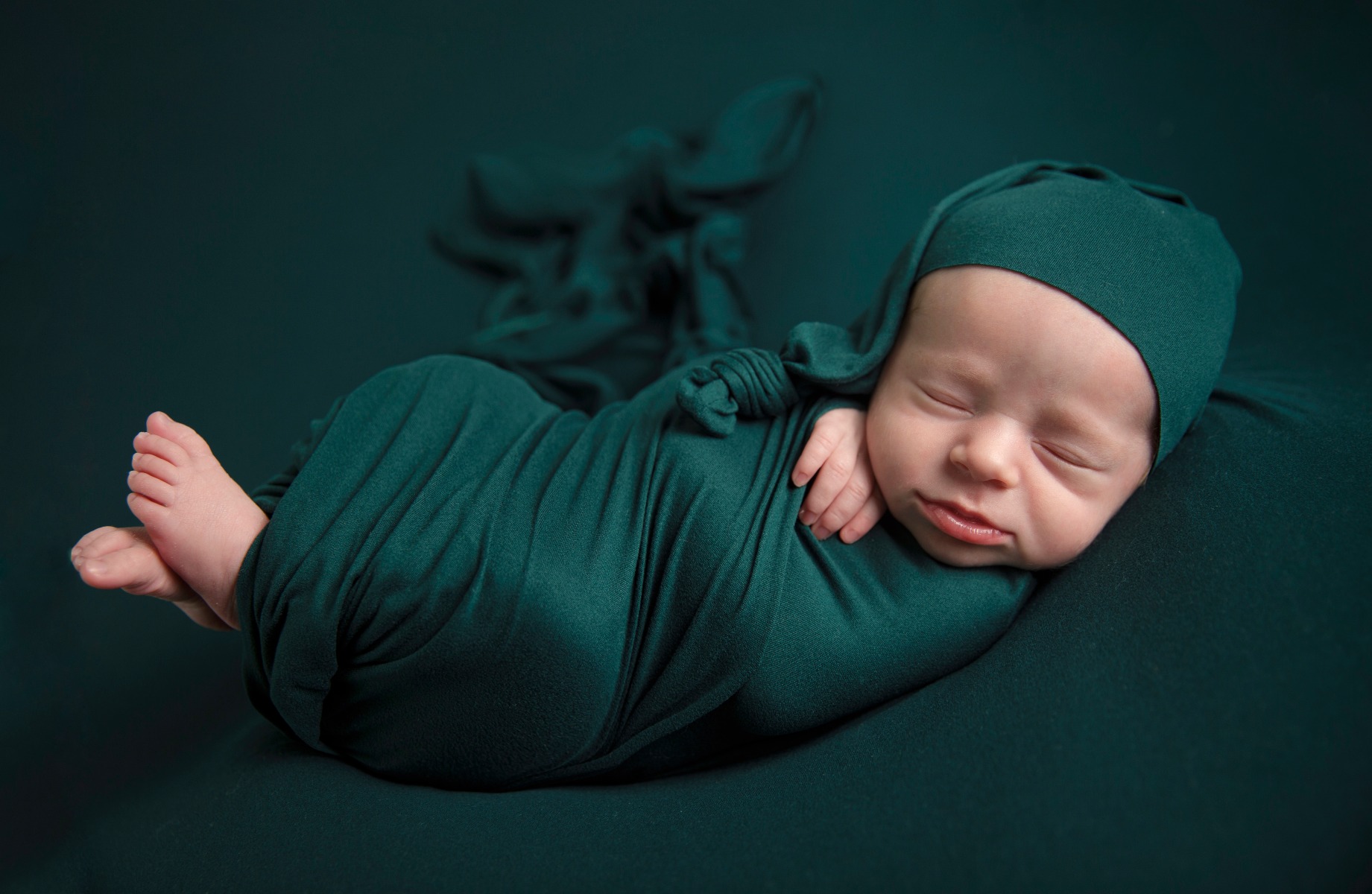 newborn baby swaddled in a deep green with a swaddle cap