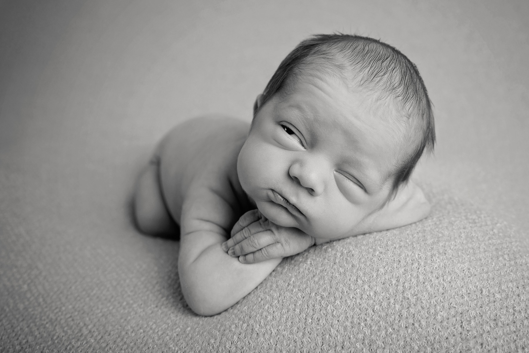 newborn baby peeks open one eye in his sleep