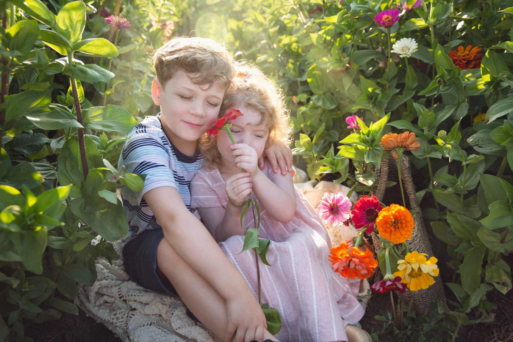 two young children snuggle in a flower field of zinnias