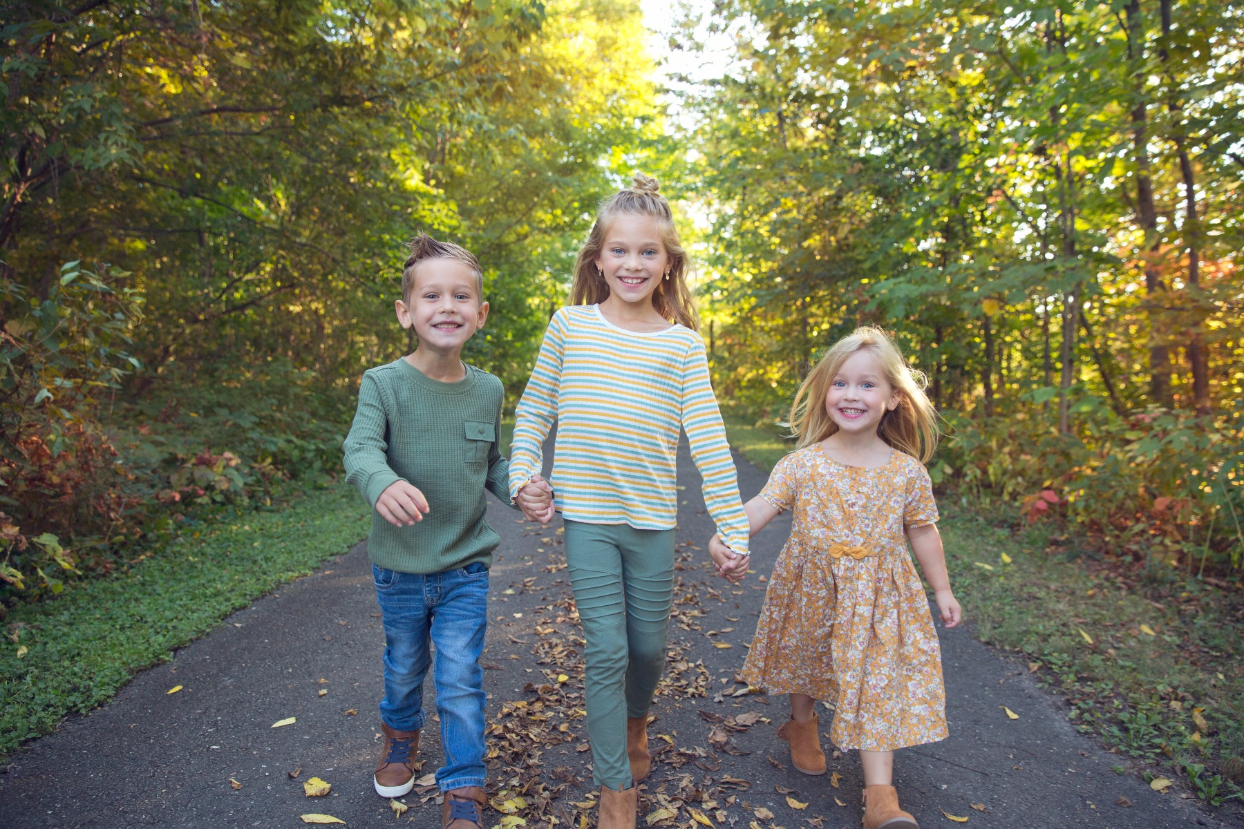 three siblings walk together on a fall path