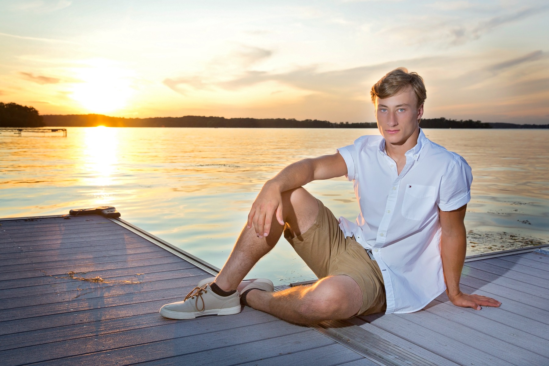hs senior boy sits on a dock by a sunset