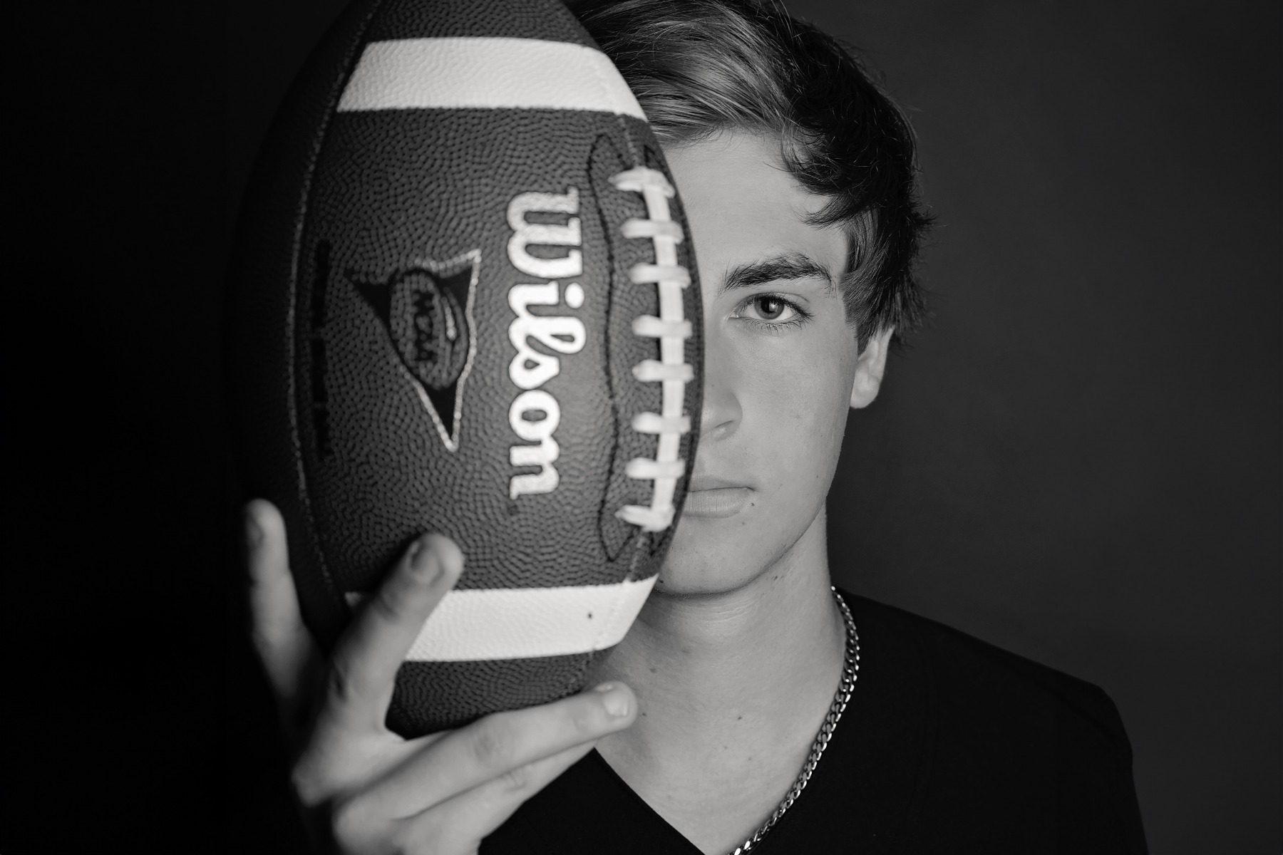 hs senior boy in B&W with a football over half of his face